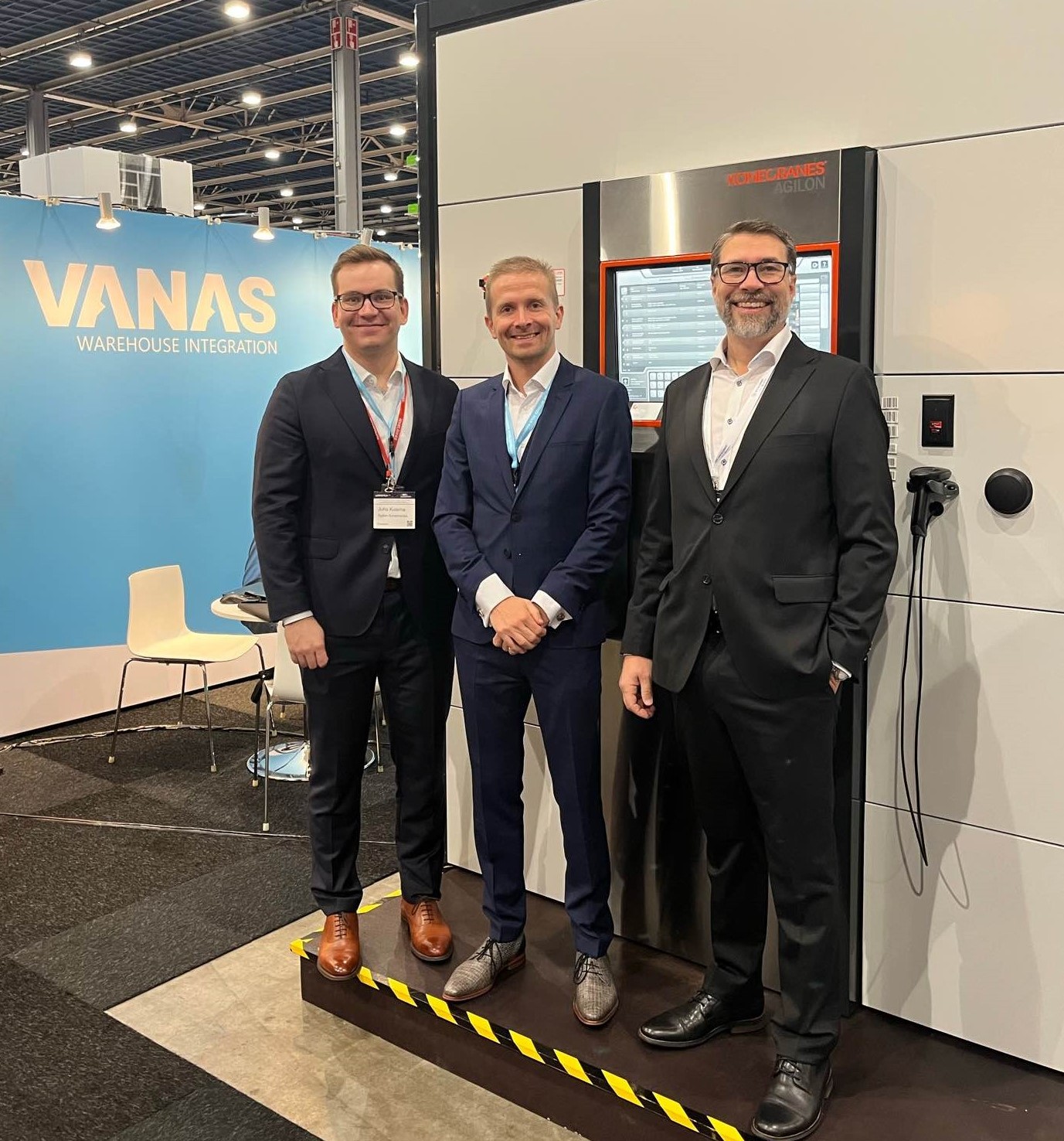 Three smiley hosts in suits standing in front of Agilon exhibition demo