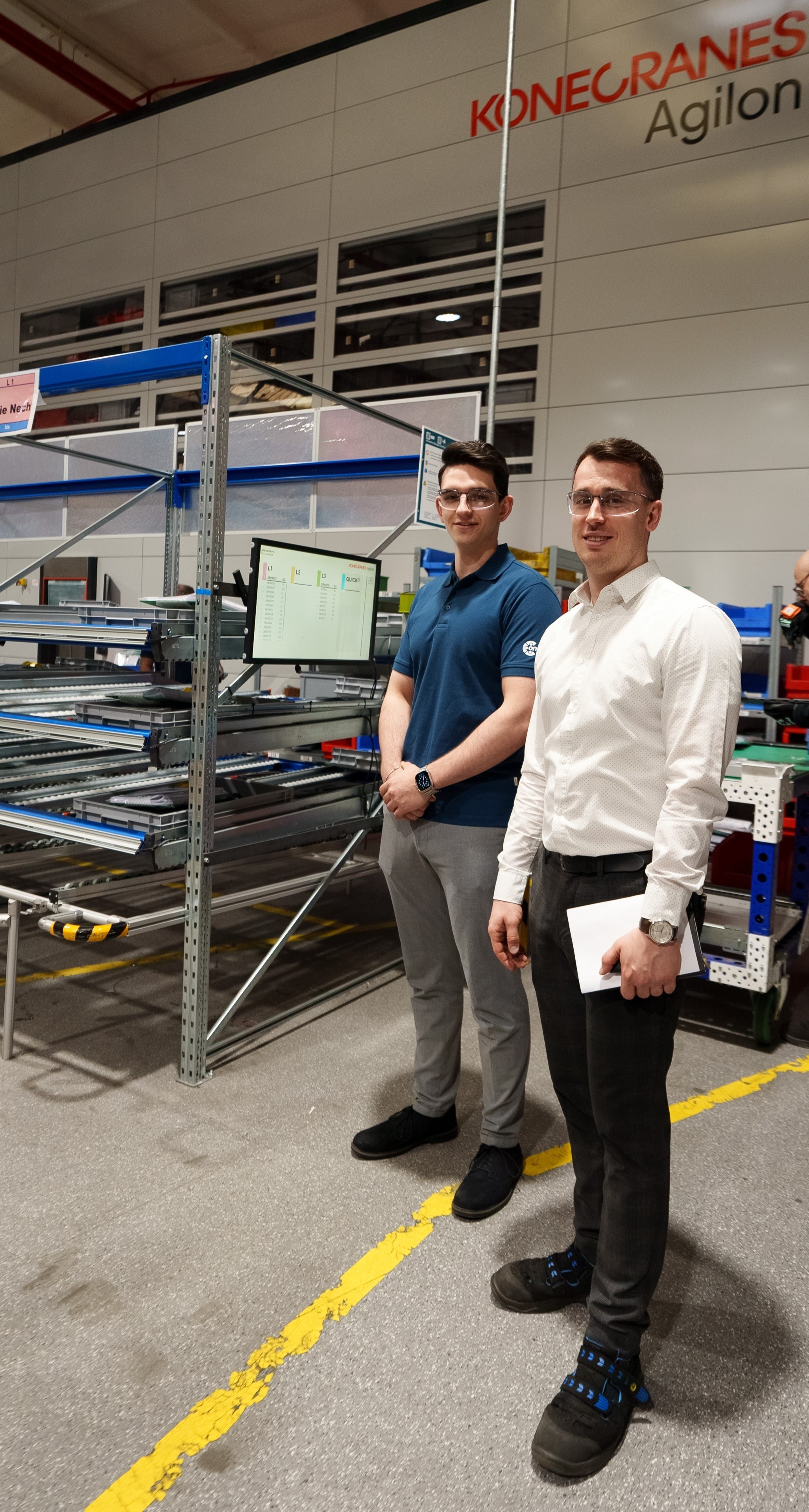 Tim Lüchtemeier and Lars Beckonert from Demag stand in front of the Agilon system at the Wetter production site. Lars is positioned in the background on the left and Tim on the right front