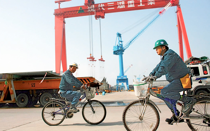 Workers ride bikes by Goliath gantry crane