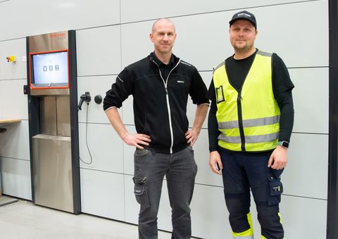 Happy Valmet employees, one with safety vest and other with black jacket in front of the Valmet´s automated warehouse Agilon