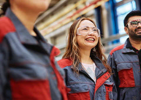 Three persons standing in Konecranes branded working clothes and wearing safety glasses
